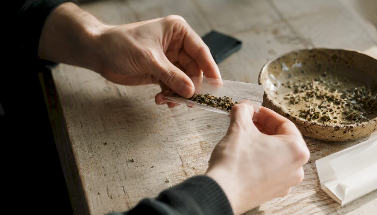 Hände drehen einen Joint aus Hanf und Kräutern.